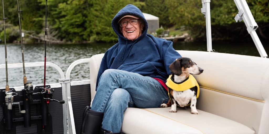 Senior man and a dog enjoying a pontoon boat tour on a lake in autumn.