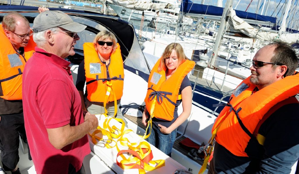 A senior sailing instructor is briefing a crew about the safety equipment.