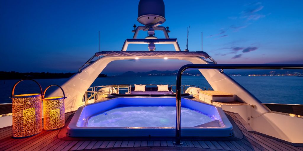 A luxury yacht with lights and a hot tub sailing in the sea at night
