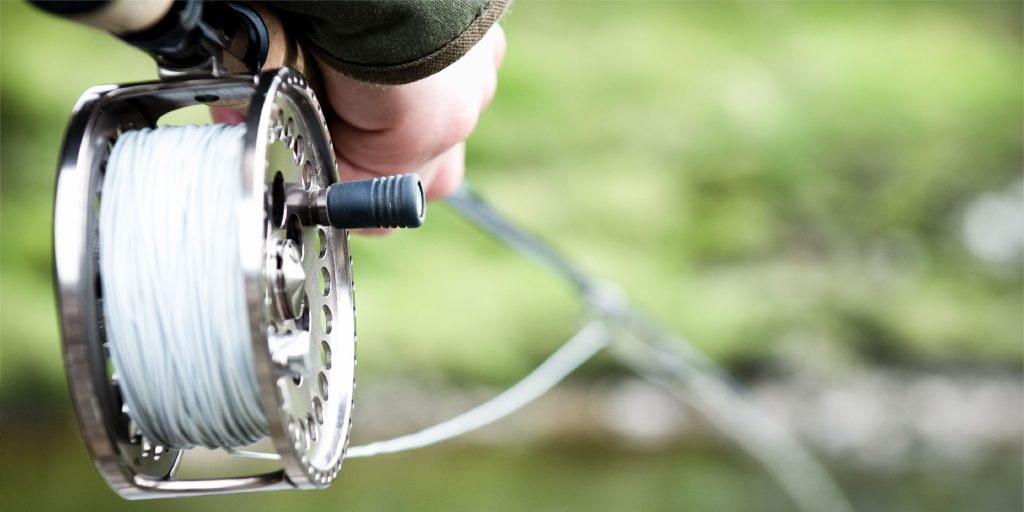 Close-up on a fishing reel as the rod is held out over the river