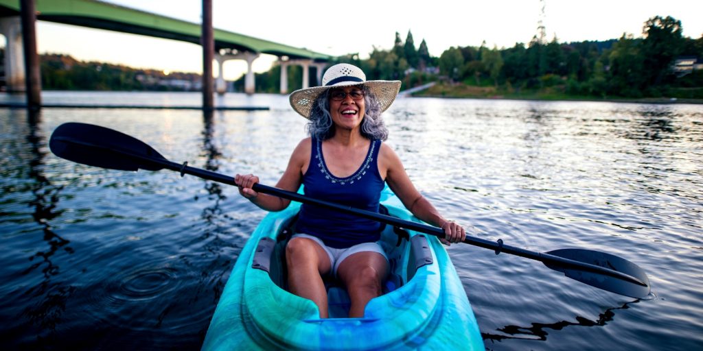 Cute smiling elderly woman wearing a hat and kayaking