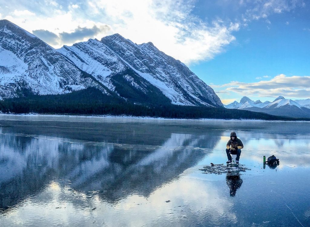 Man ice fishing near mountains